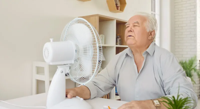 An older man keeping cool with a fan in warm weather